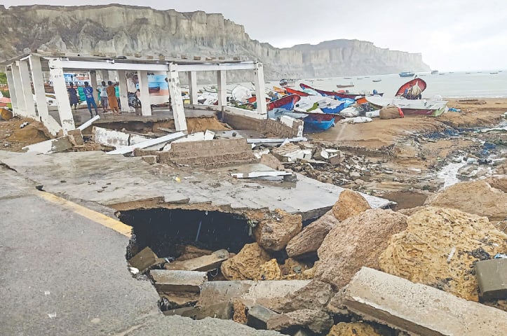  GWADAR: Fishermen gather under a broken structure on the shore along a badly damaged road, as boats are stacked near the jetty following heavy rainfall in Balochistan, on Thursday.—AFP 